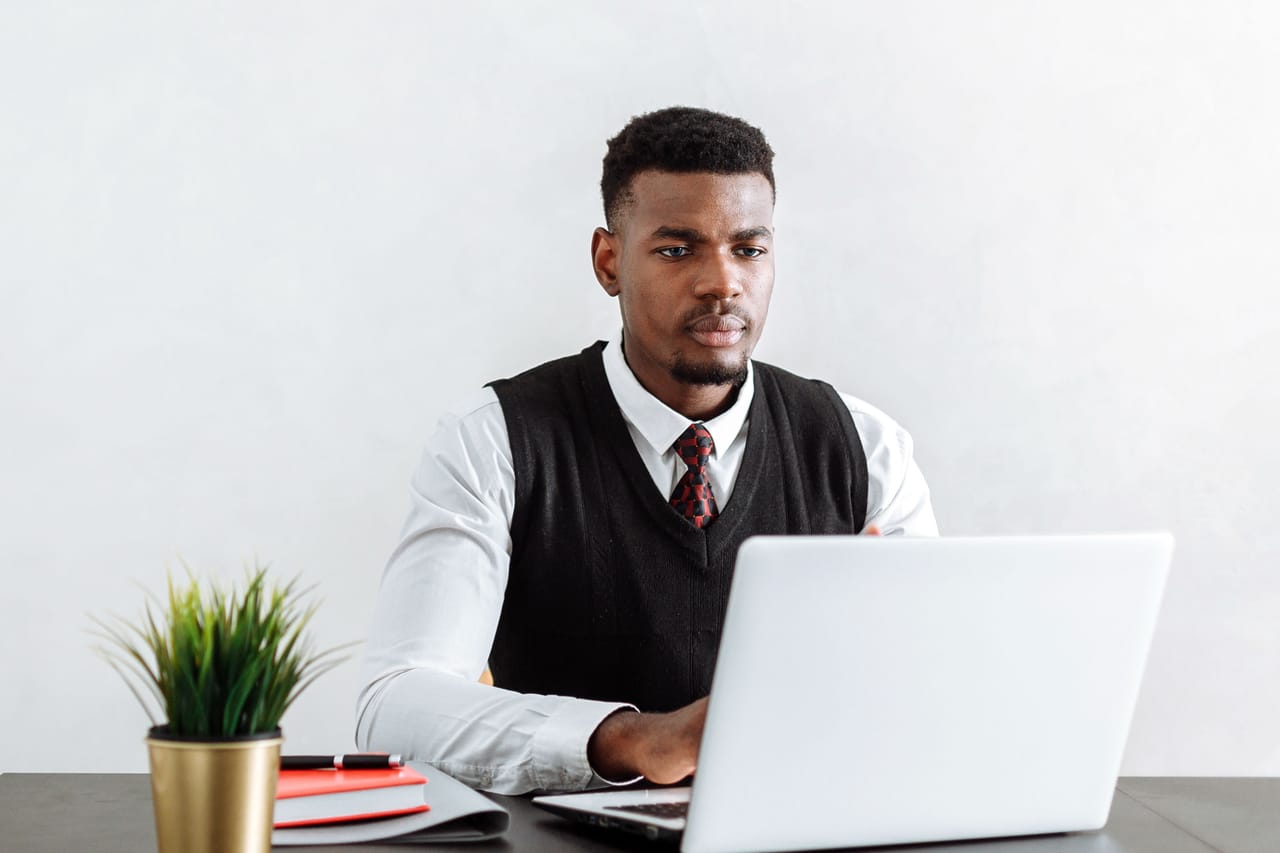 A man in a shirt, tie, and sweater vest working on a laptop at a desk